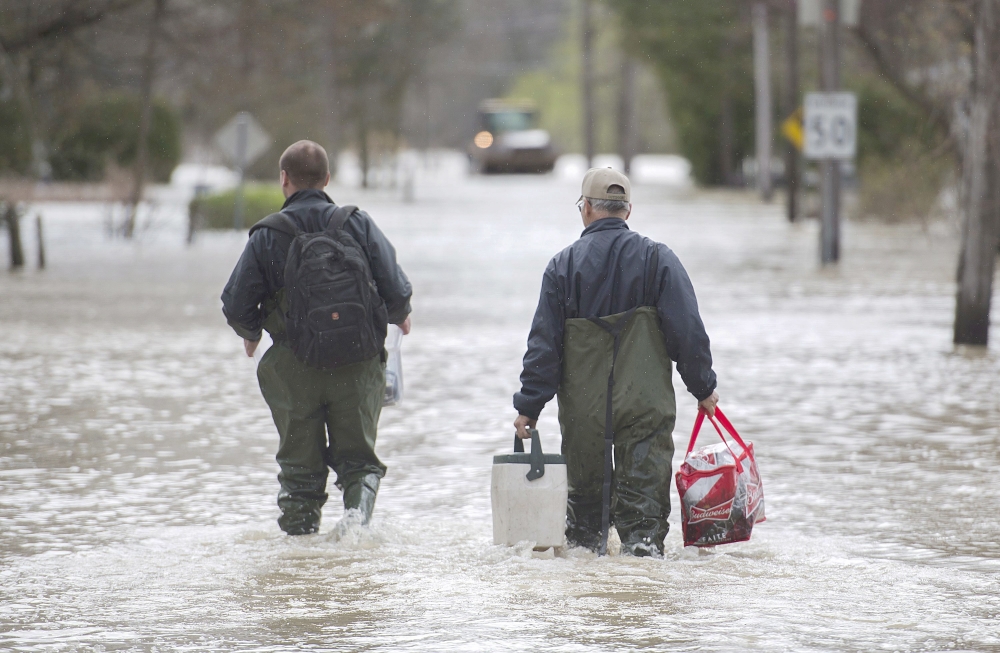 Two men carry belongings along a flooded street in the town of Rigaud west of Montreal, Canada, on Sunday. — AP