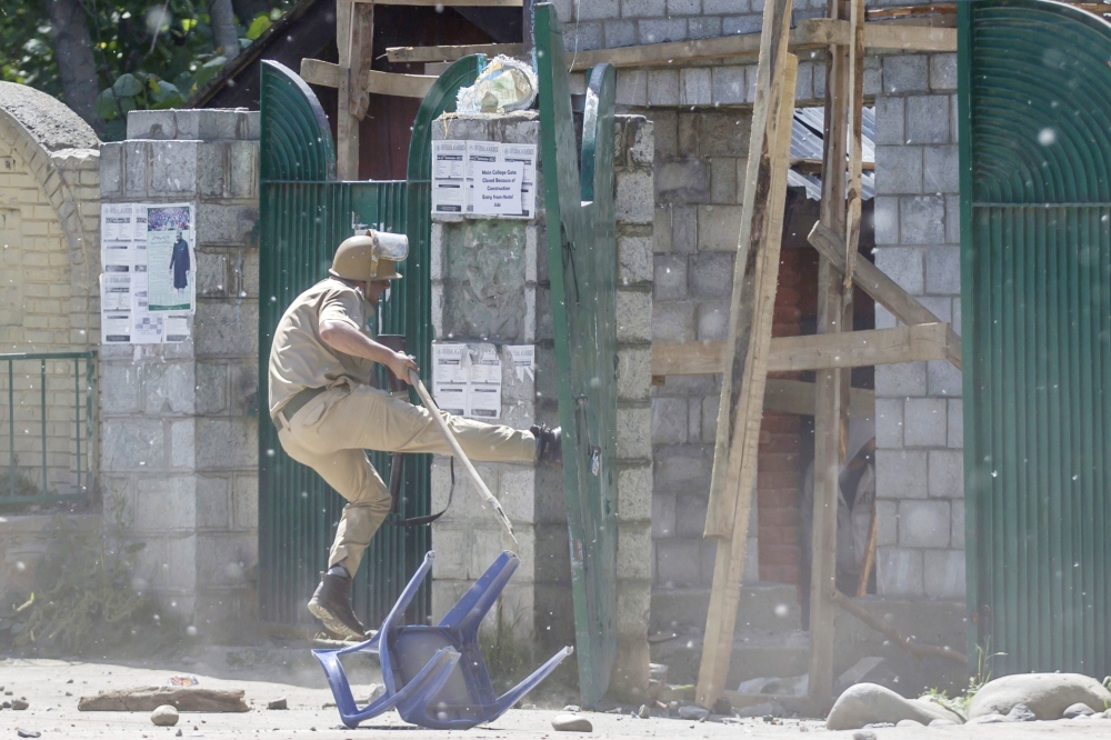 An Indian policeman kicks the gate of a college during a clash with Kashmiri students in Srinagar, Indian controlled Kashmir, on Tuesday. — AP