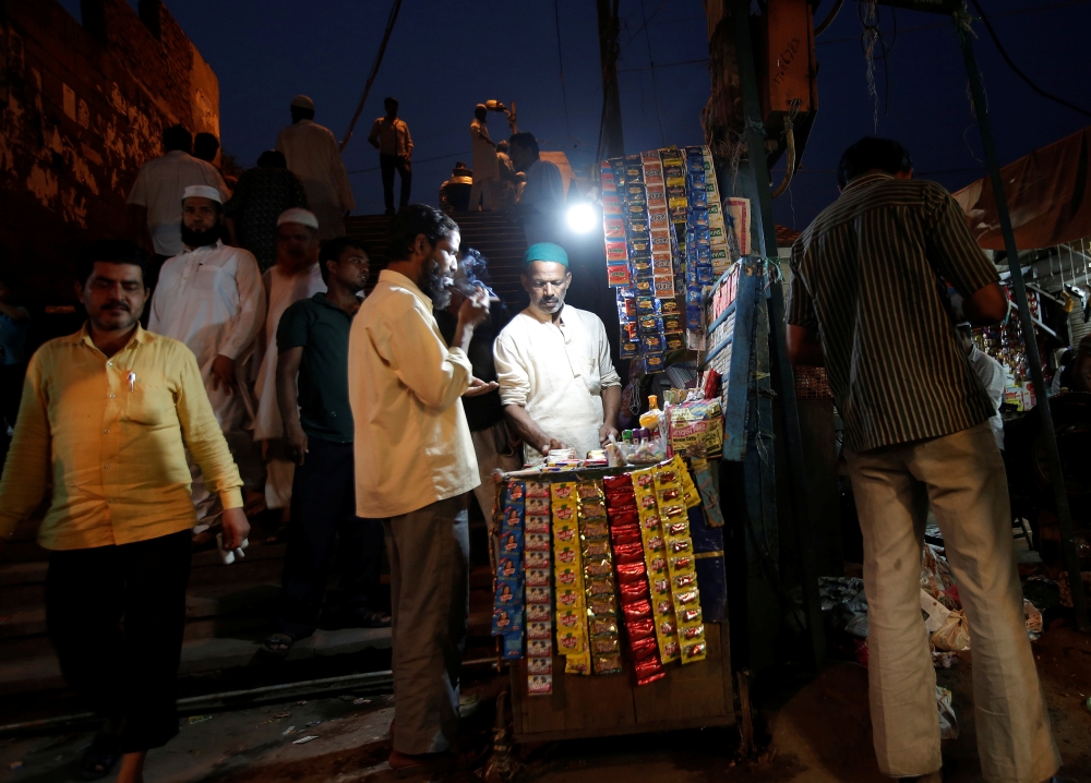 A man lights a cigarette at a roadside stall in the old quarters of Delhi, India. - Reuters