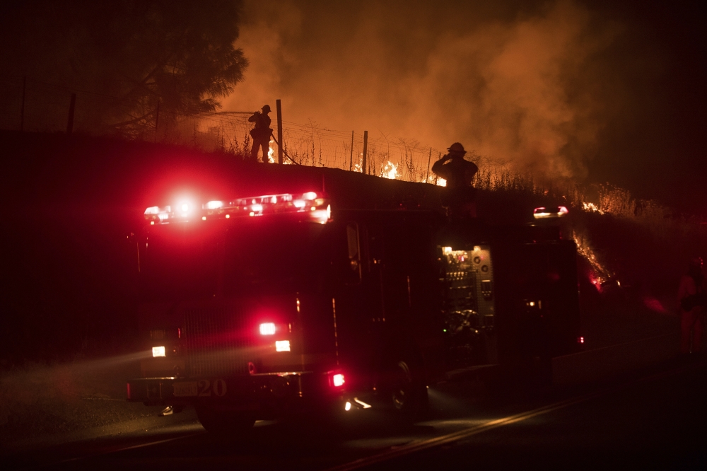 A firefighter sprays water on a back fire while battling the wildfires near Mariposa, California, on Tuesday. — AP