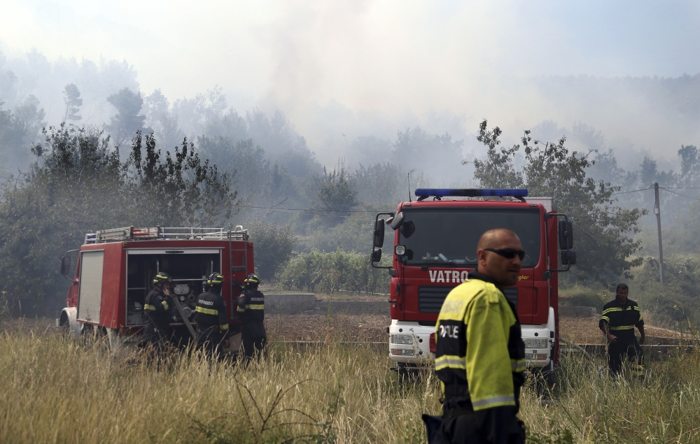 Firefighters gather near their trucks after controlling a fire in the village of Srinjine, southern Croatia, on Tuesday. — AP