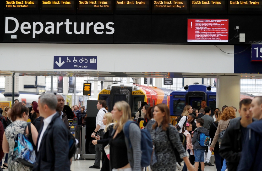 Passengers walk past a screen warning of disruption on one of the main railway lines into Waterloo station in central London on Monday. — Reuters