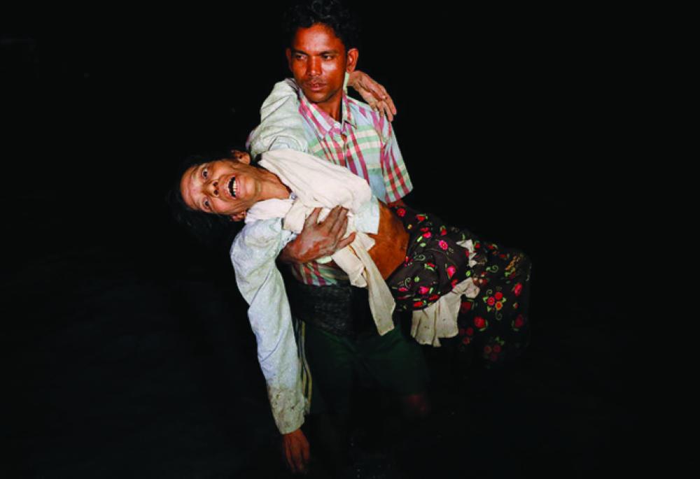 A Rohingya carries his elderly relative under the cover of darkness from Myanmar to Bangladesh. — Reuters
