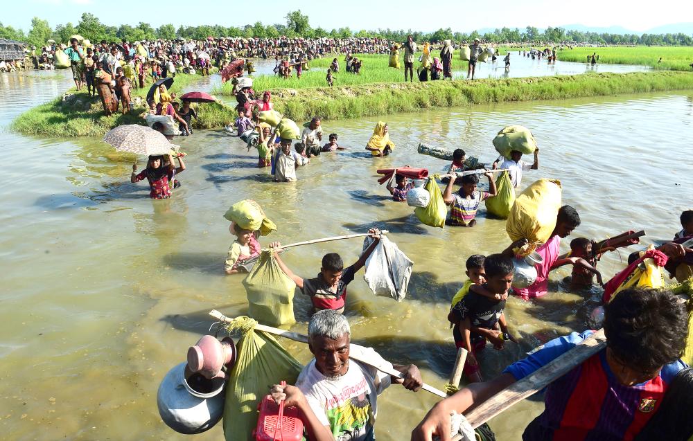 Rohingya refugees walk through a shallow canal after crossing the Naf River as they flee violence in Myanmar to reach Bangladesh in Palongkhali near Ukhia on Monday. — AFP
