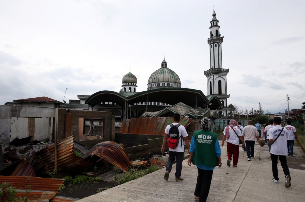 Local government workers walk past a damaged house as they clear the area inside a war-torn in Marawi city, southern Philippines. — Reuters photos