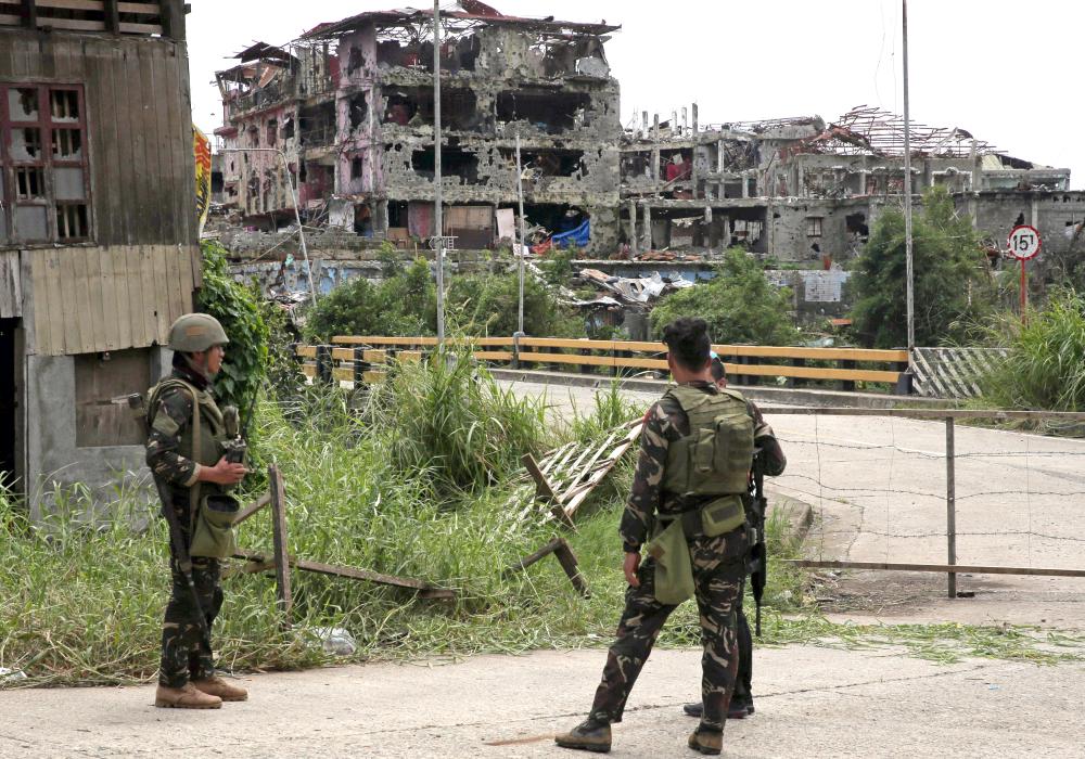 Soldiers stand on guard and look at damaged buildings and houses after government troops cleared the area from militant groups inside the war-torn area in Saduc proper, Marawi city, southern Philippines on Sunday. — Reuters