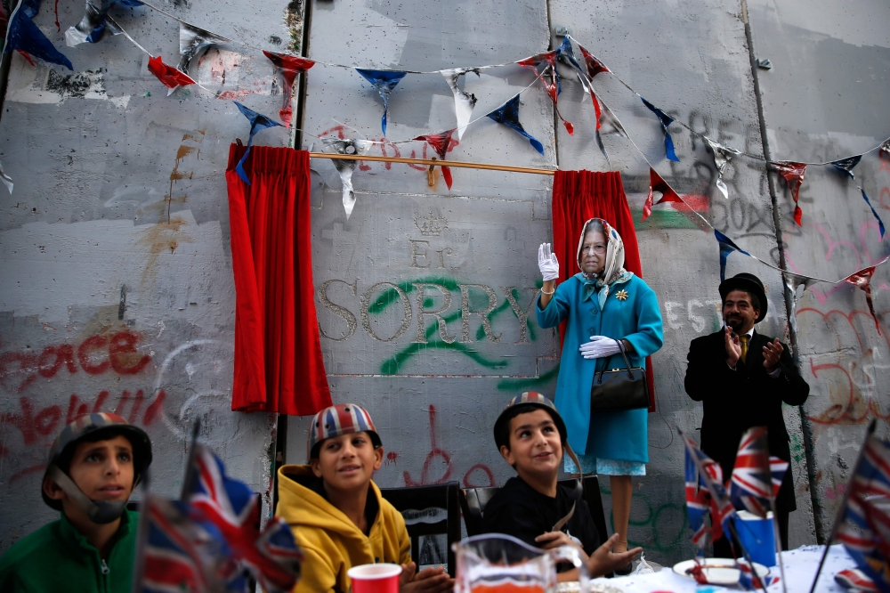 An actor dressed up as Queen Elizabeth and Palestinian children from the Al-Aida refugee camp attend an event held by secretive British street artist Banksy to apologize for the 100th anniversary of the Balfour Declaration on Wednesday at his Walled-Off Hotel in Bethlehem in the occupied West Bank. - AFP
