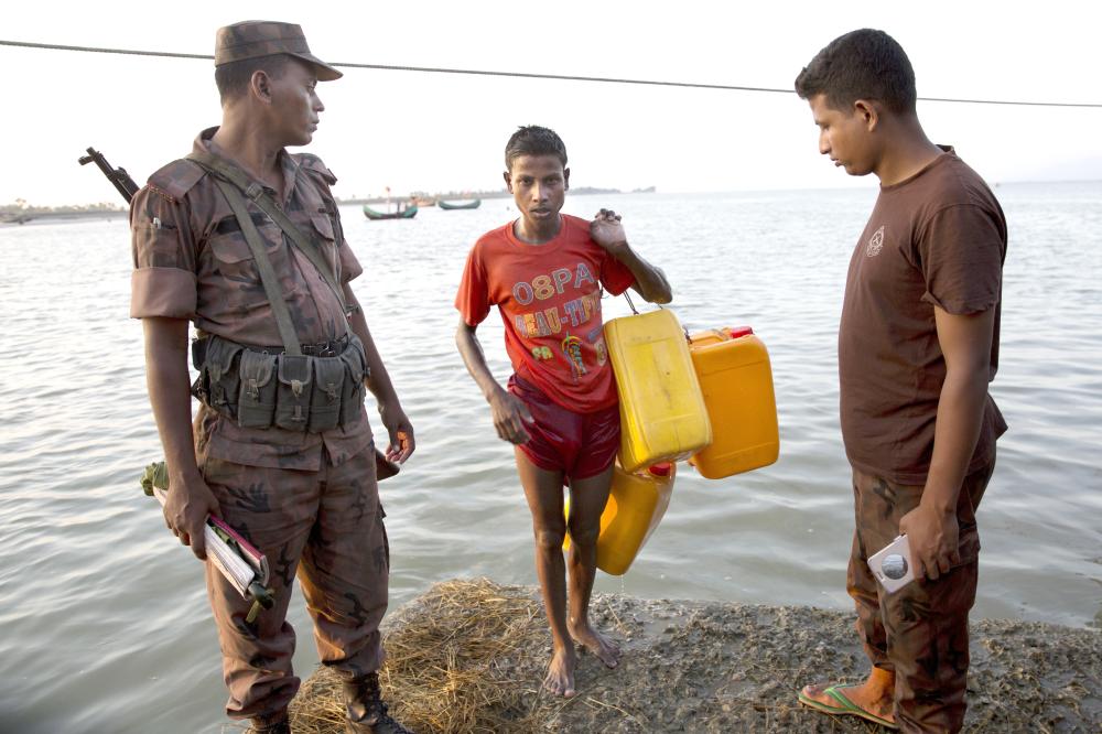 A Bangladeshi border guard, left, looks at a Rohingya Muslim Belal Hussain, 15, center, as he steps out of the water carrying yellow plastic drums he used as a flotation aid at Shah Porir Dwip, Bangladesh, after swimming the Naf river in this Nov. 4, 2017 photo. — AP