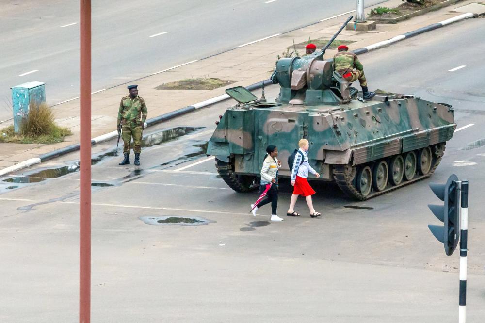 Young women walk past an armored personnel carrier that stations by an intersection as Zimbabwean soldiers regulate traffic in Harare on Wednesday. — AFP