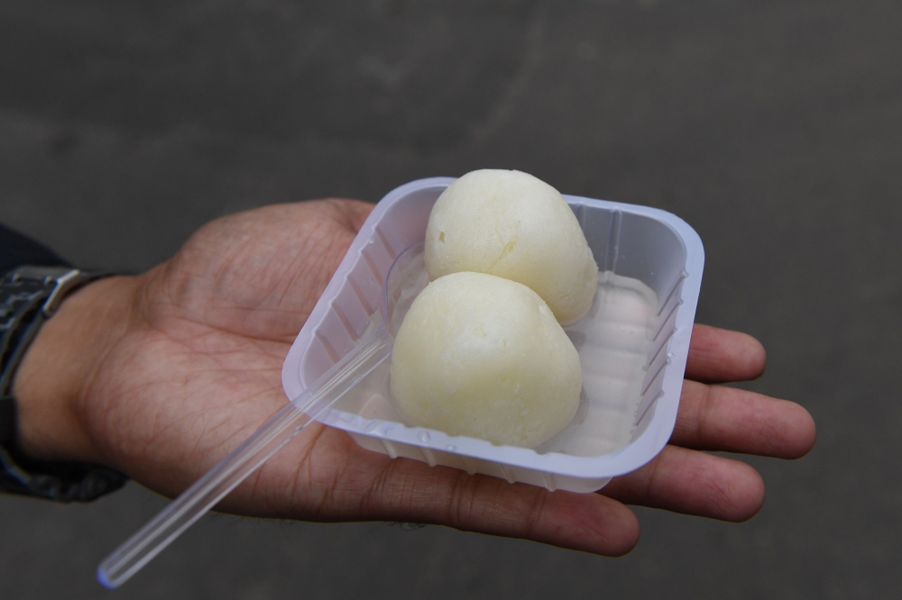 An Indian man holds a bowl of rasgulla dessert on a street in New Delhi on Wednesday. - AFP