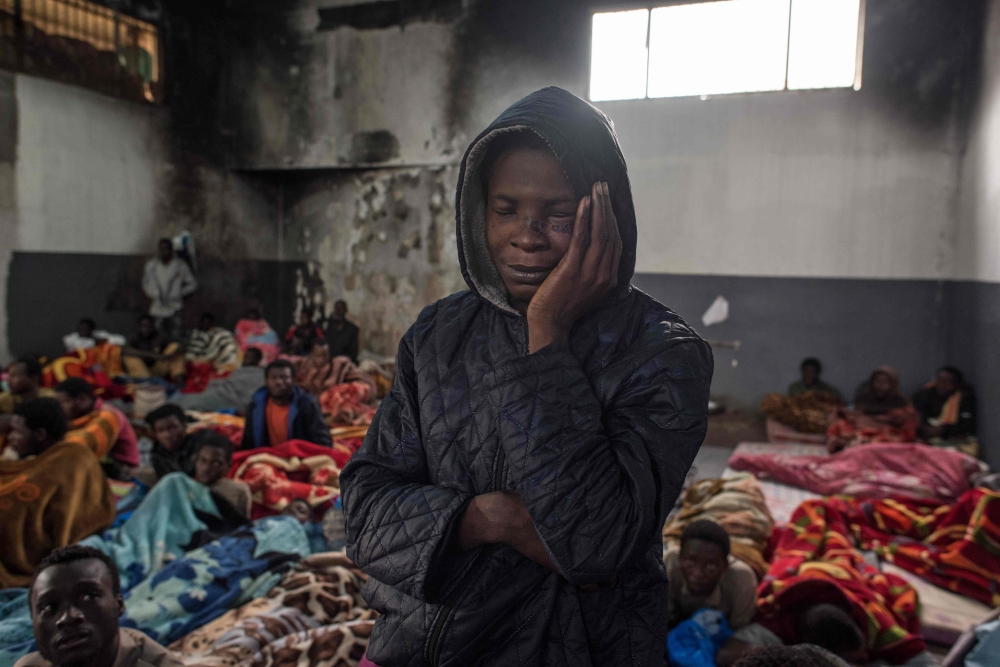 A migrant holds his head as he stands in a packed room at the Tariq Al-Matar detention center on the outskirts of the Libyan capital Tripoli. — AFP