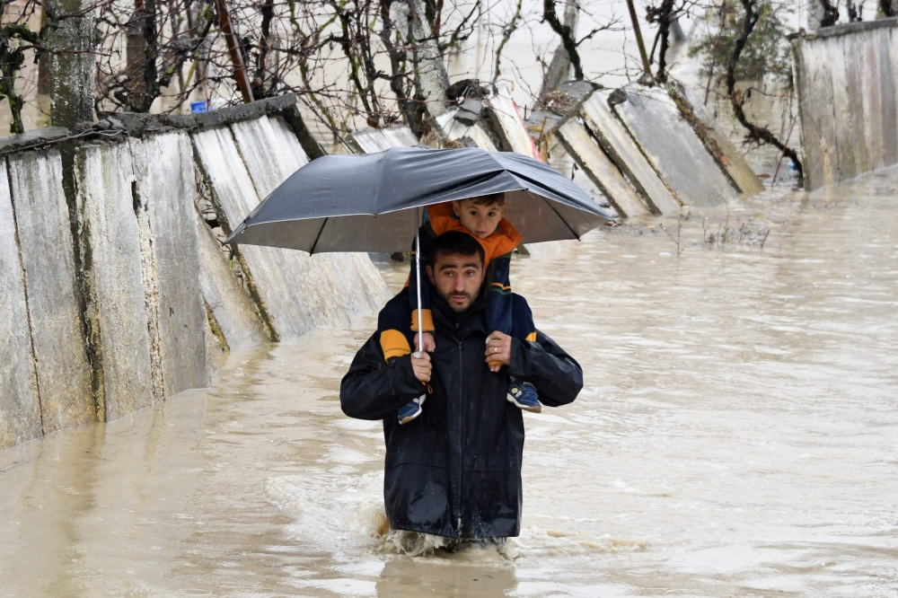 A man carries a child on his shoulders as he walks in a flooded street while leaving their houses in the village of Hasan, near Fushe Kruje, north of the capital Tirana, Albania, on Friday. — AFP