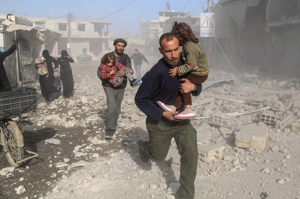 Syrians make their way through debris following a reported air strike in the rebel-held town of Beit Sawa, in the eastern Ghouta region on the outskirts of the capital Damascus. — AFP