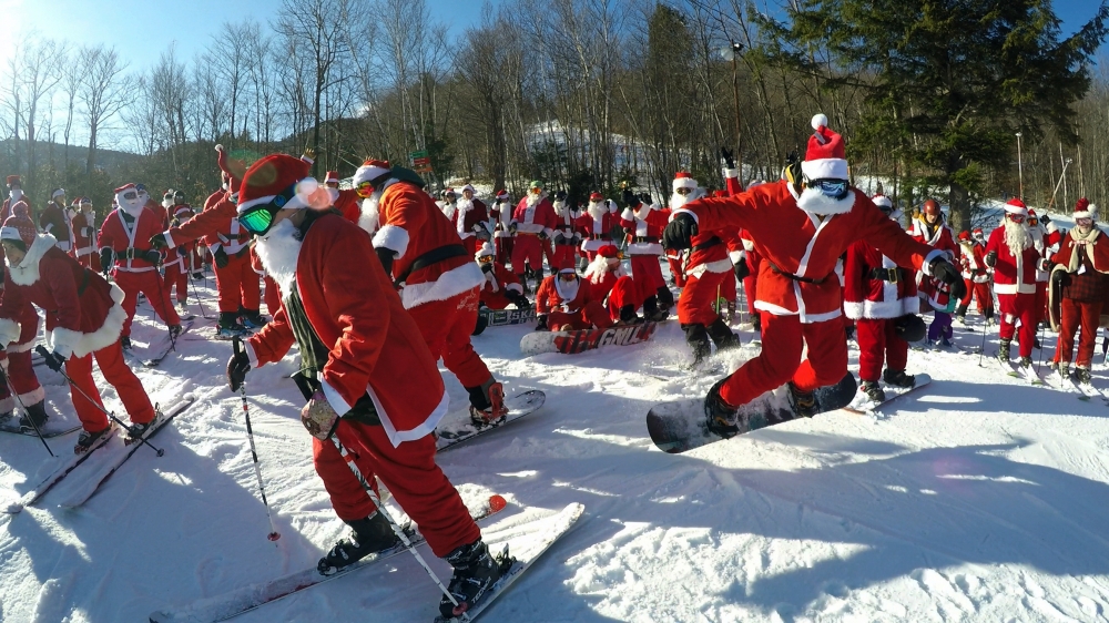 A snowboarder, right, gets a jump start as 160 Santas head down a slope at Sunday River during the ski resort's 18th annual Santa Sunday event in Newry, Maine. - AP
