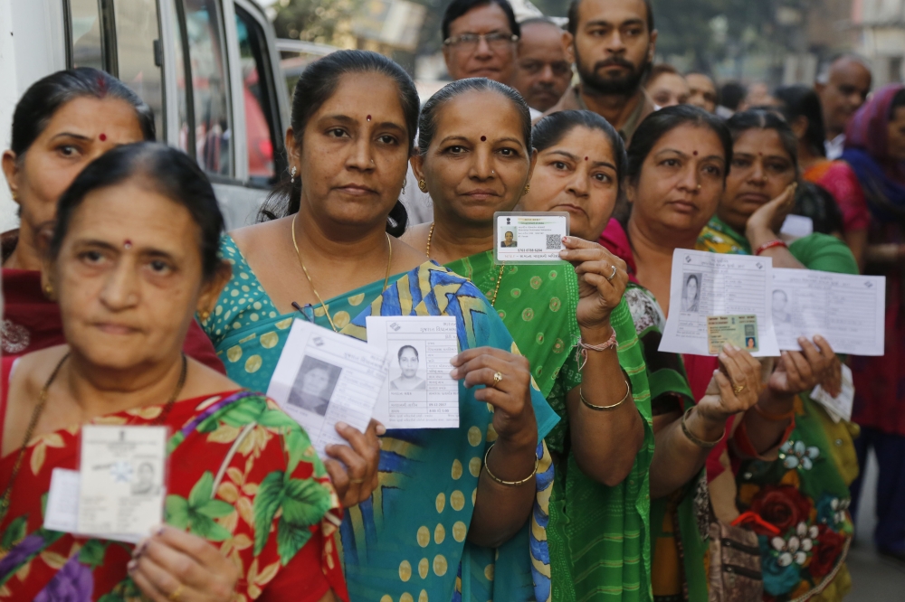 Women display their voter identity cards as they wait to cast their vote during the first phase of the Gujarat state assembly election in Rajkot, India, on Saturday. — AP
