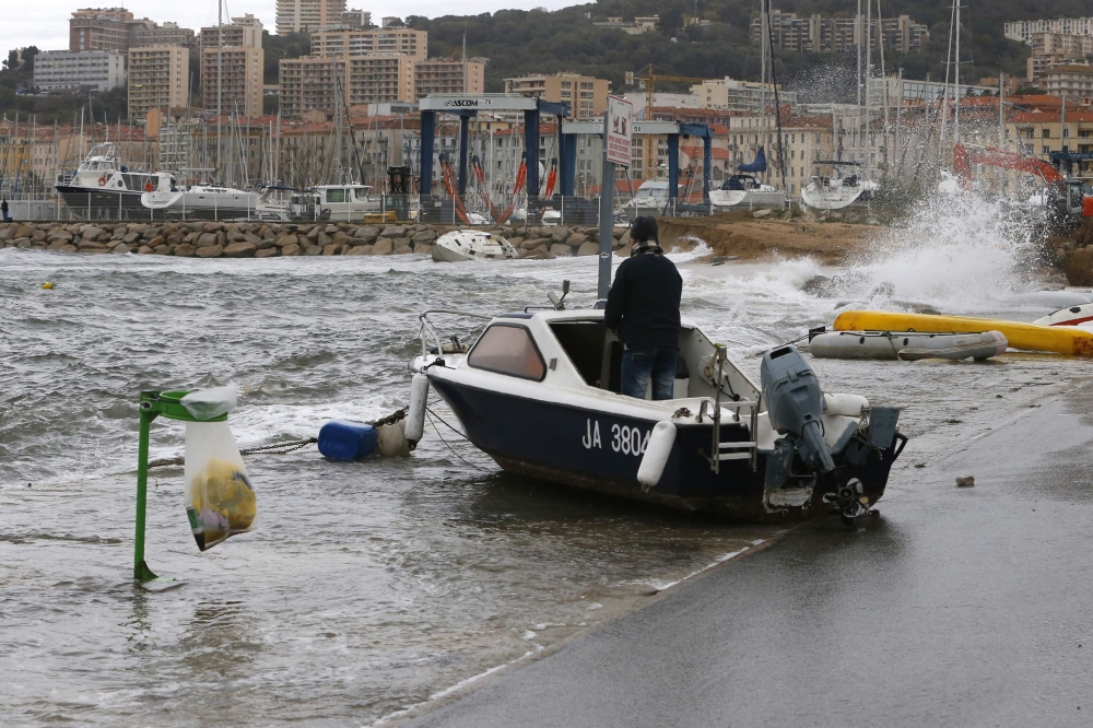 A man stands on his boat, pushed onto the dock by waves, in Ajaccio, on the French Mediterranean Island of Corsica, on Monday. — AFP