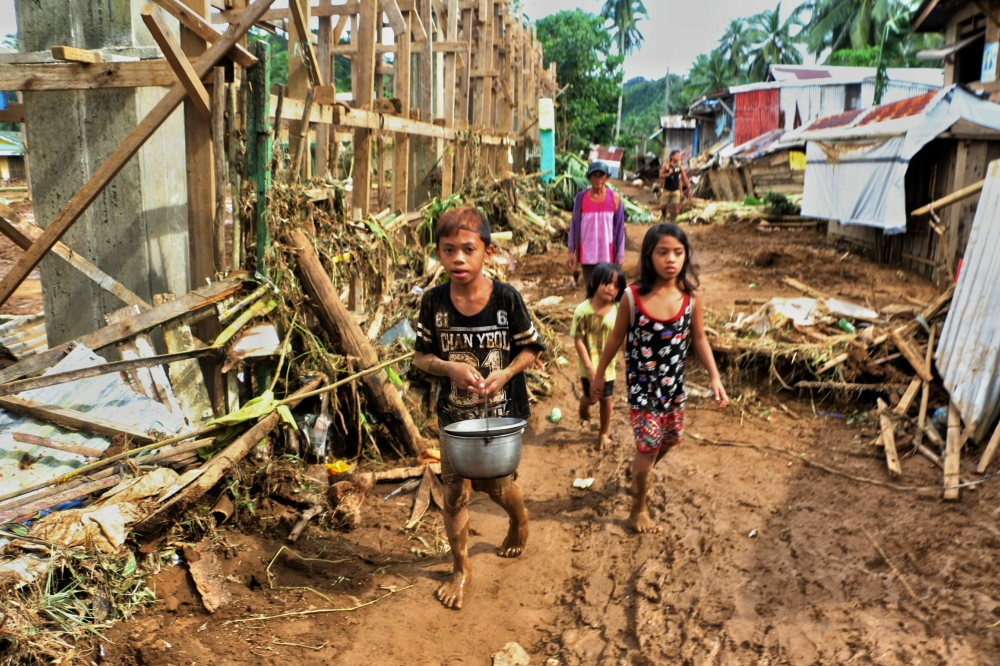 Children walk past debris and damaged houses trees in Barangay San Mateo Borongan in eastern Samar on Sunday, after Tropical Depression Kai-Tak blew through the area. — AFP