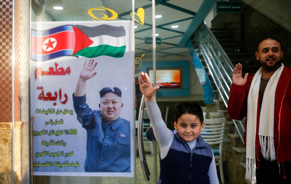 Salam Rabaa (L), the Palestinian owner of Rabaa restaurant and his son gesture with their right hands imitating a poster of North Korean leader Kim Jong-Un, at the gate of the venue premises in the Jabalia refugee camp in the northern Gaza strip. — AFP