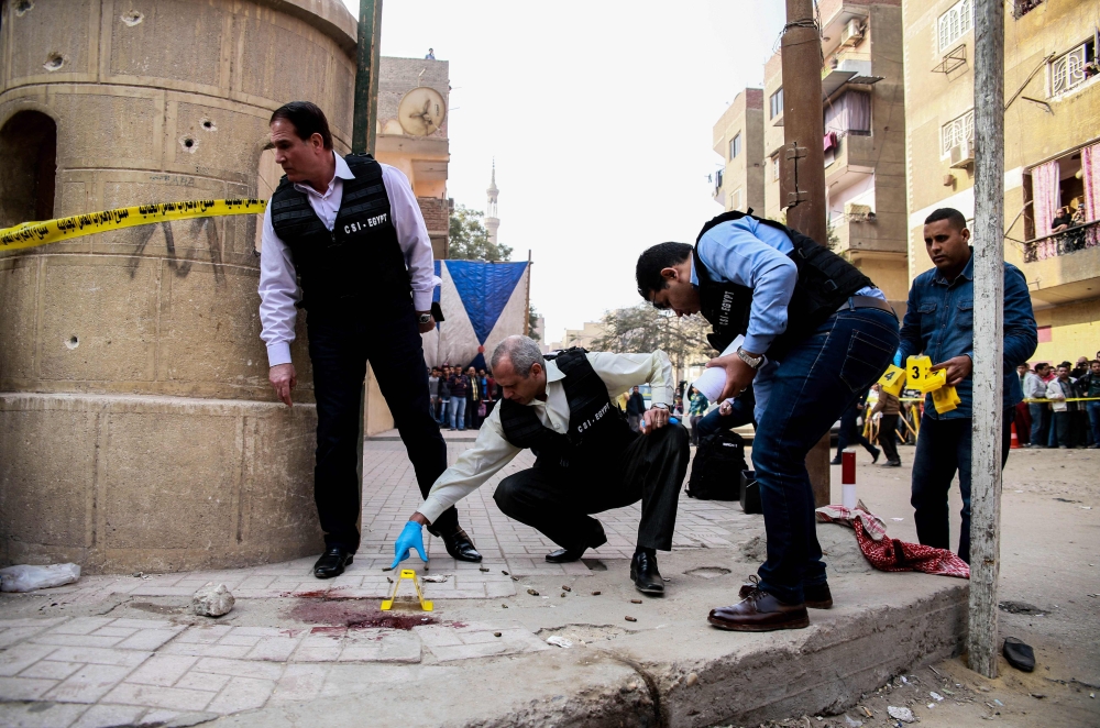 Egyptian security members and forensic police inspect the site of a gun attack outside a church south of the capital Cairo on Friday. — AFP