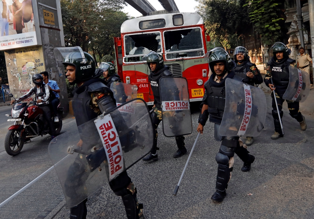 Riot police walk past a damaged public bus during a protest in Mumbai, India, on Tuesday. — Reuters