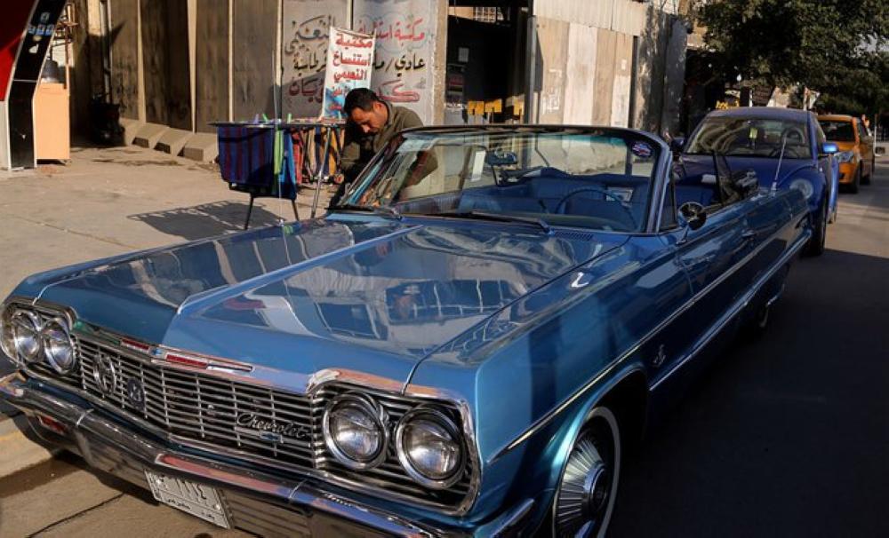 A man cleans a blue 1964 Chevrolet parked in front of the owner Saad Al-Nuaimi's coffee shop in the northern Azamiyah neighborhood of Baghdad, Iraq. — AP