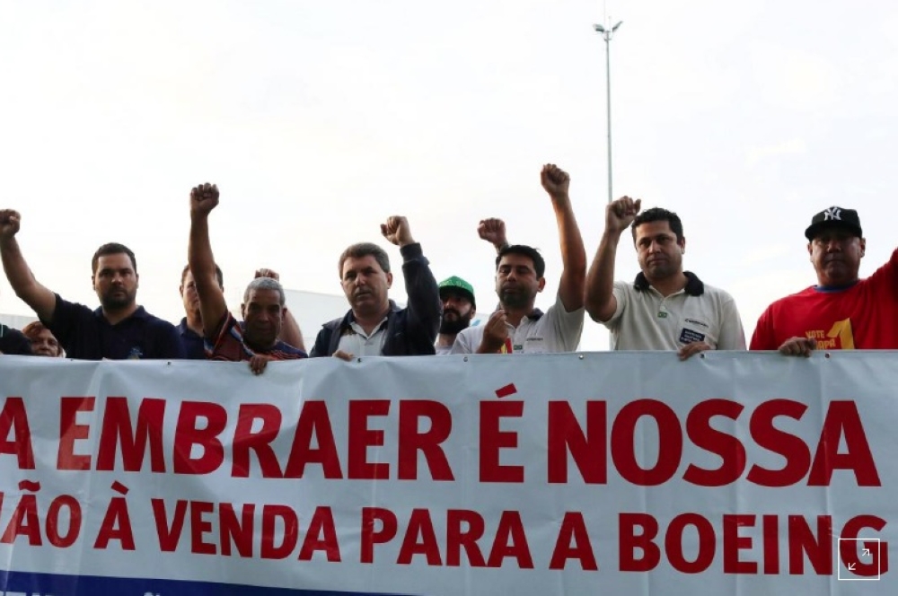 Employees of Embraer hold a banner that reads: 