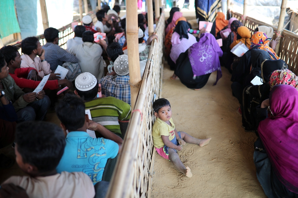 A Rohingya child sits on the floor while his mother waits in a queue to collect aid supplies in Kutupalong refugee camp in Cox's Bazar, Bangladesh, on Sunday. — Reuters