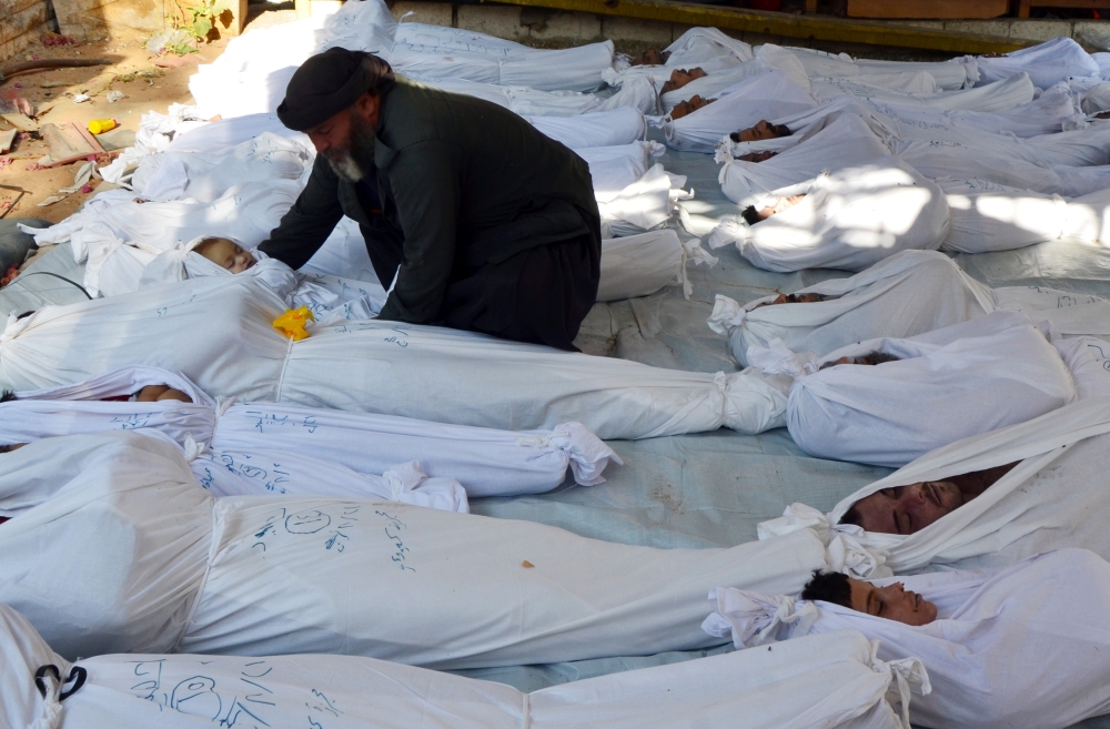 This file photo shows a man holds the body of a dead child among bodies of people activists say were killed by nerve gas in the Ghouta region, in the Duma neighborhood of Damascus, Syria, on Aug. 21, 2013. — Reuters