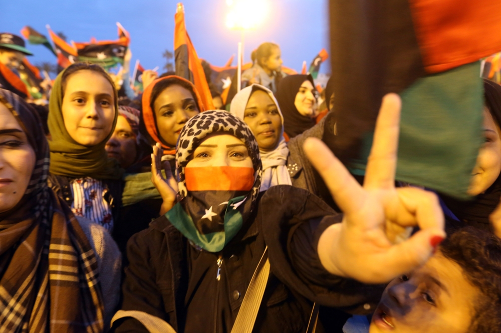 A Libyan woman flashes the victory gesture while others wave national flags as they attend a celebration marking the 7th anniversary of the Libyan revolution which toppled late leader and strongman Moammar Gaddafi, in the capital Tripoli's Martyrs Square. — AFP