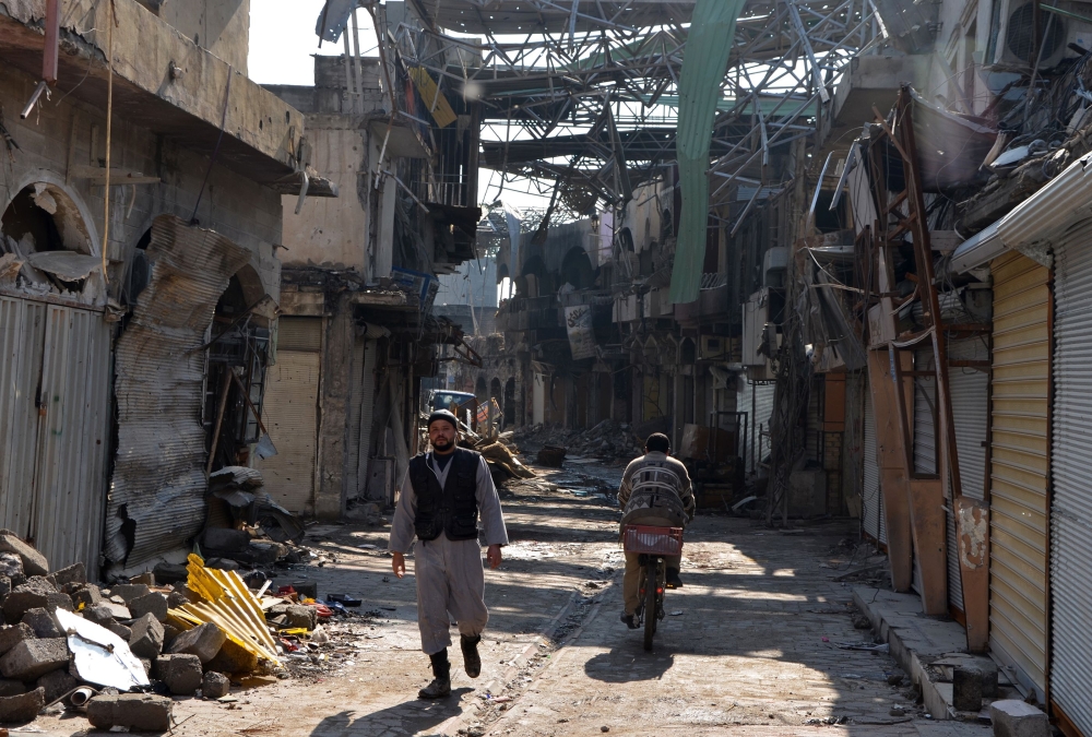 A general view shows Iraqis walking along a damaged street in the northern Iraqi city of Mosul. — AFP