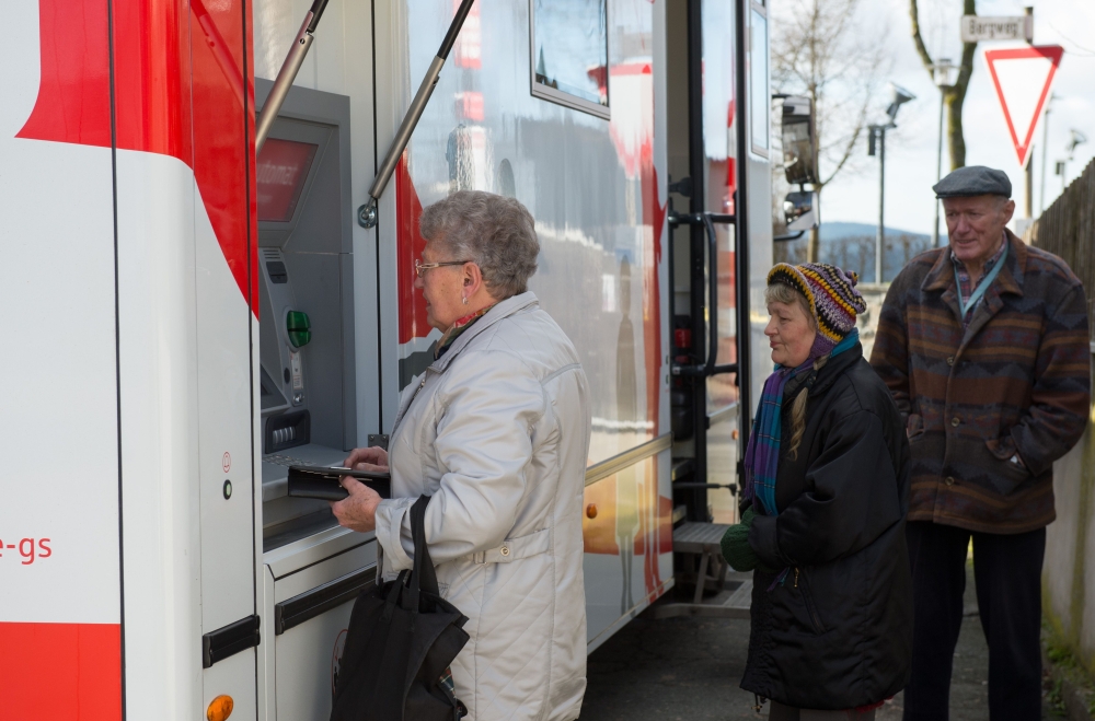 A customer withdraws money from a cash machine at a mobile office bus of the savings bank Sparkasse in Tschirn, southern Germany. Bank manager Juergen Schaller never expected to end up getting a trucker's license and driving 20,000 kilometers per year. - AFP