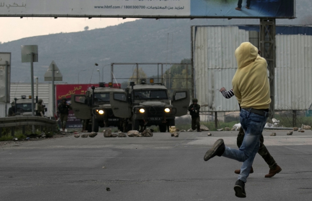 A Palestinian demonstrator throws a rock at Israeli forces during clashes near the Hawara checkpoint, south of the West Bank city of Nablus. — AFP