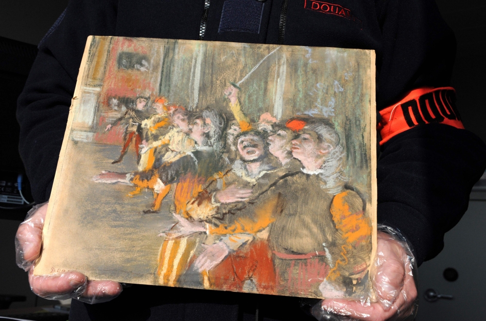 This handout photo shows a French customs officer holding a Degas painting stolen from a museum in Marseille nine years ago. The painting was found on a bus near Paris. - AFP
