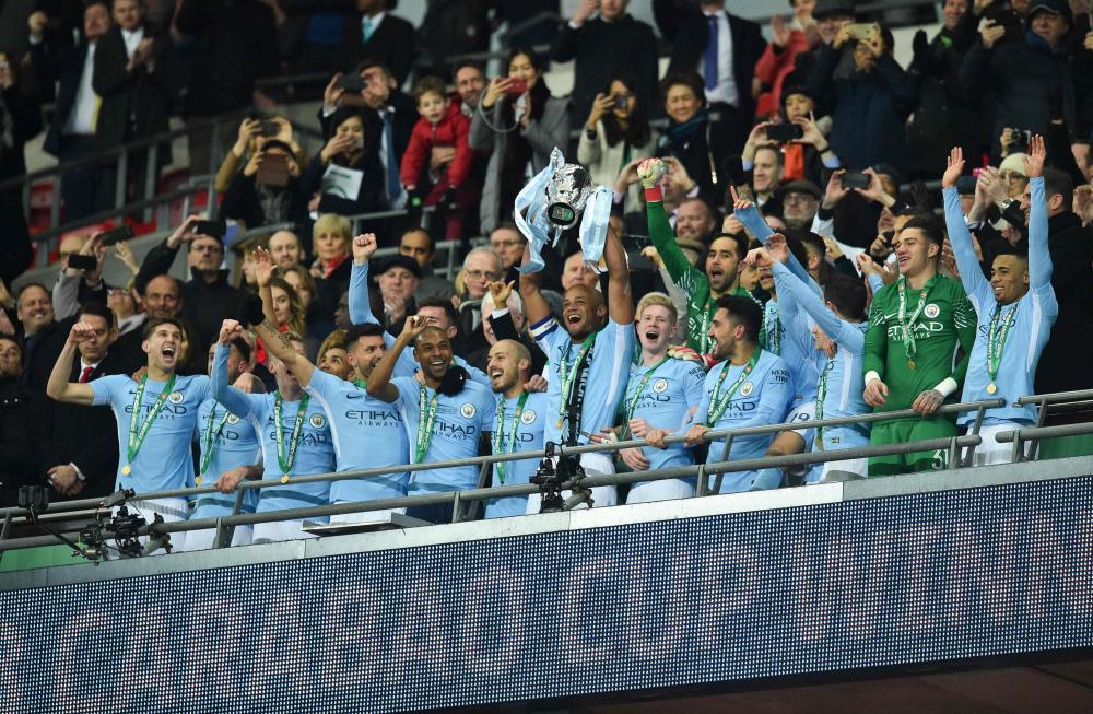 Manchester City's Vincent Kompany lifts the trophy with teammates after their victory in the English League Cup final against Arsenal at Wembley Stadium in north London Sunday. — AFP