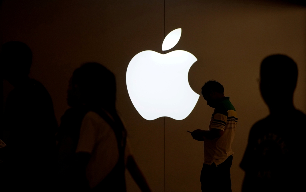 A man looks at his mobile phone in front of an Apple logo outside its store in Shanghai, China. - Reuters
