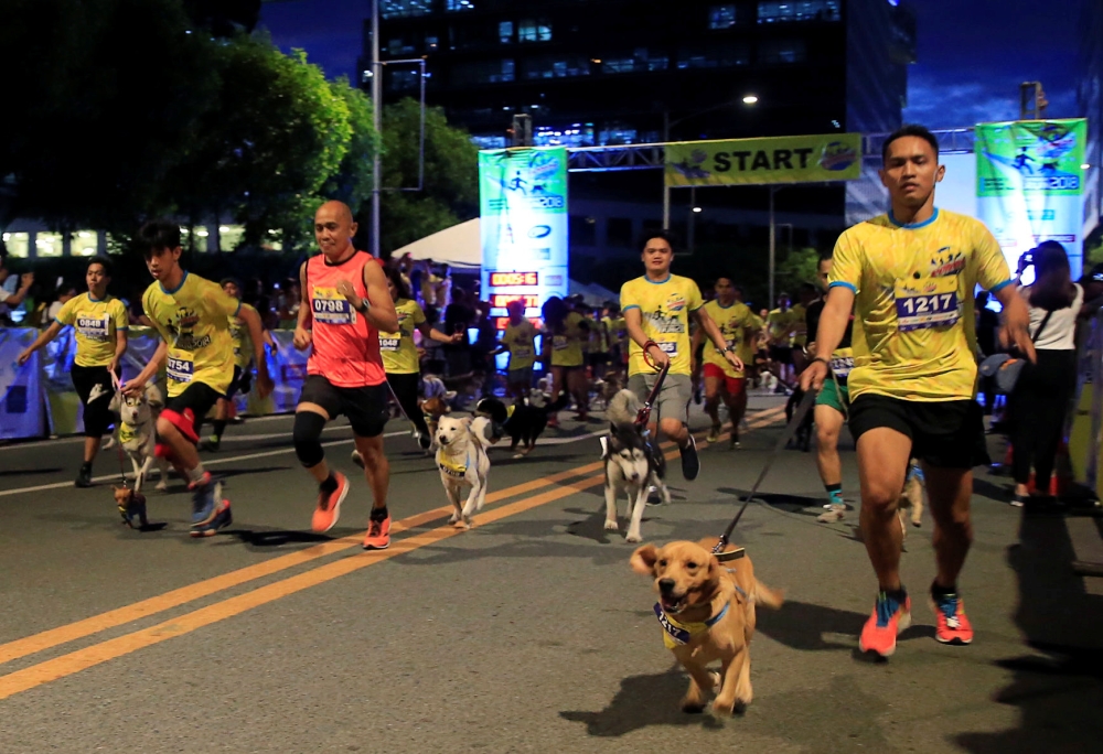 Dog owners and their pets jog through an open road as they participate in the annual Doggie Run outside a mall in Pasay city, metro Manila, Philippines on Saturday. - Reuters