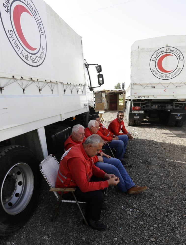 Employees of the Syrian Arab Red Crescent wait next to vehicles carrying aid at the Al-Wafideen checkpoint on the outskirts of Damascus neighboring the rebel-held Eastern Ghouta region. — AFP