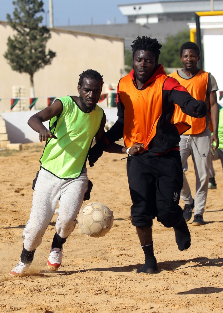 Cameroonian (orange) and Senegalese (yellow) African migrants, split into two teams, take part in a football match at the Libyan Interior Ministry's illegal immigration shelter in Tajoura. — AFP