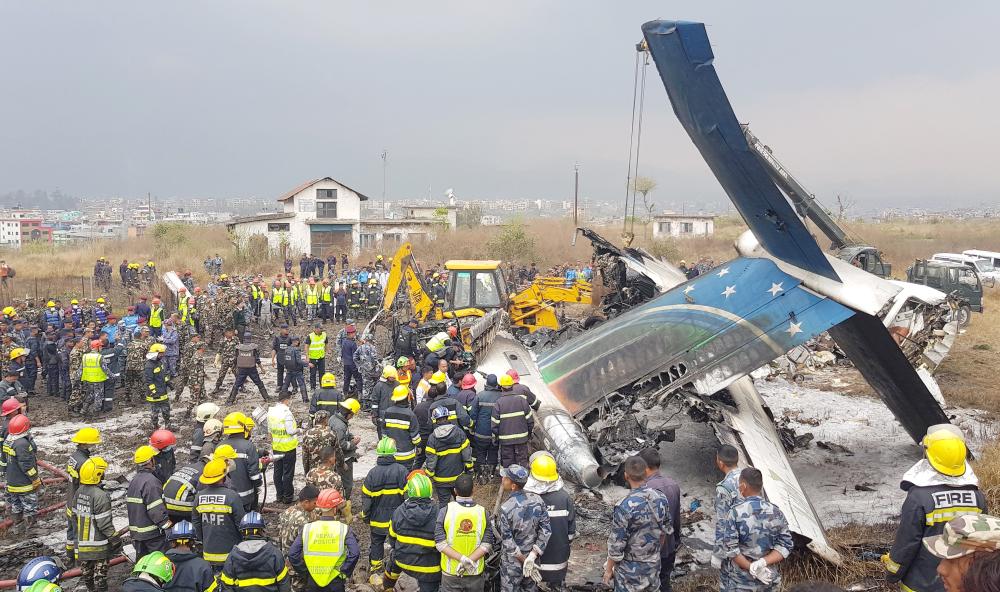 Nepali rescue workers gather around the debris of an airplane that crashed near the international airport in Kathmandu on Monday. — AFP