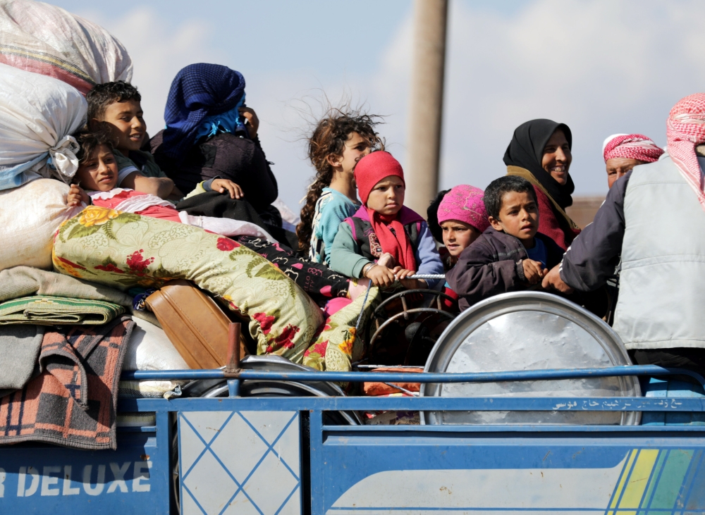 Internally displaced people ride on the back of a truck with their belongings in the town of Inab, eastern Afrin. — Reuters