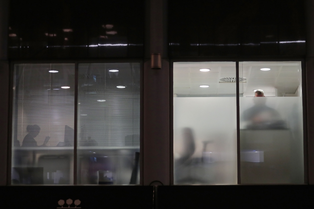 People are seen through blinds searching inside the offices of Cambridge Analytica in central London on Friday evening, just hours after a judge approved a search warrant of the offices. — AFP