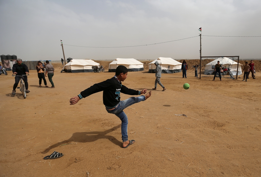 A Palestinian kicks a ball near a tent city along the Israel border with Gaza, ahead of a protest demanding to return to their homeland, in the southern Gaza Strip, on Thursday. — Reuters