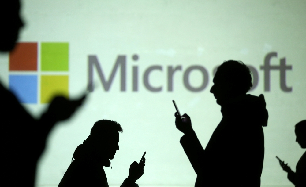 Silhouettes of mobile users are seen next to a screen projection of Microsoft logo in this picture illustration taken on Wednesday. — Reuters