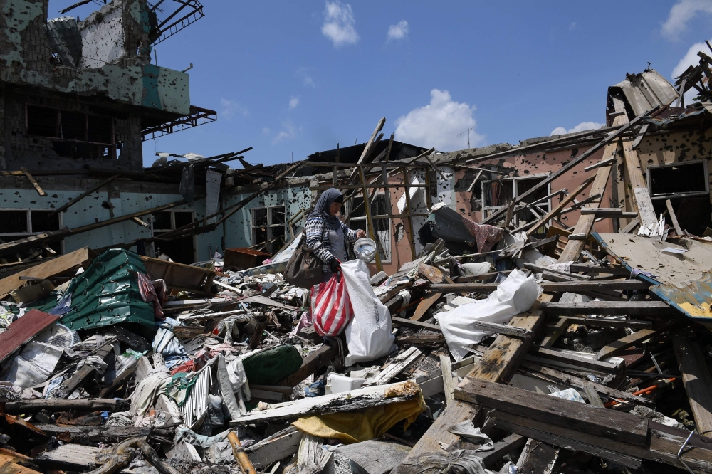 A resident collects salvageable belongings from her destroyed house during a visit to the main battle area in Marawi City, in southern island of Mindanao on Sunday. After fleeing for their lives nearly a year ago, residents of the battle-scarred Philippine city of Marawi made their first visit back on Sunday to dig through the rubble that was once their homes. — AFP