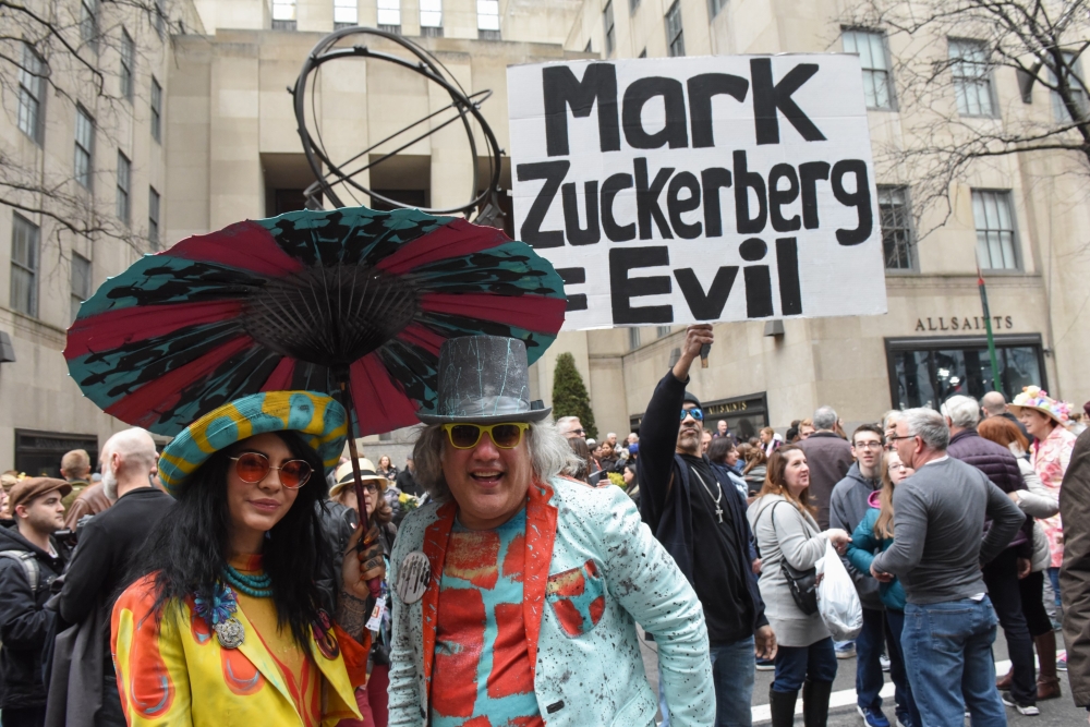 People wear Easter bonnets while a person protests against Mark Zuckerberg during the annual Easter Parade in New York City on Sunday. — AFP