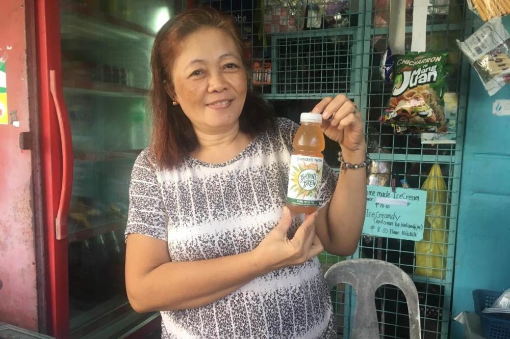 Linda Maningas holds up a bottle of Bayani Brew that she helped formulate at one of about half a dozen social enterprises that engage residents at Gawad Kalinga's Enchanted Farm in Bulacan, Philippines. - Thomson Reuters Foundation