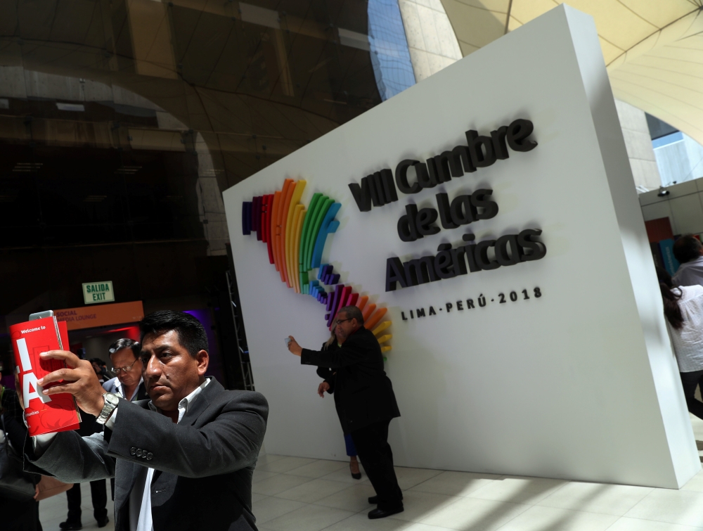 People take selfies in front of an official logo the VIII Summit of the Americas at the convention center in Lima, Peru, on Saturday. — Reuters