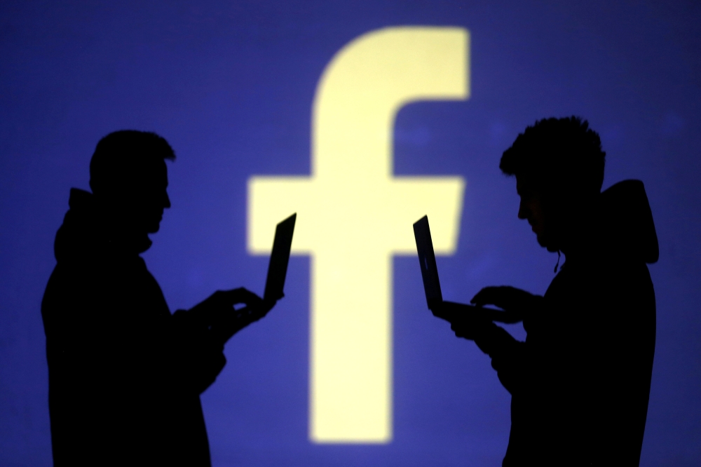 Silhouettes of laptop users are seen next to a screen projection of Facebook logo in this picture illustration taken on March 28, 2018. — Reuters