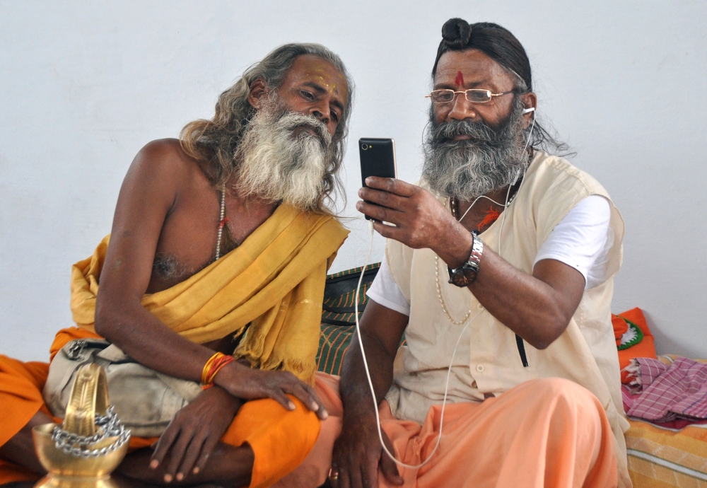 Indian sadhus look at a mobile phone as they await to register for a pilgrimage at a temple in Jammu in this June 16, 2017 file photo. — AFP