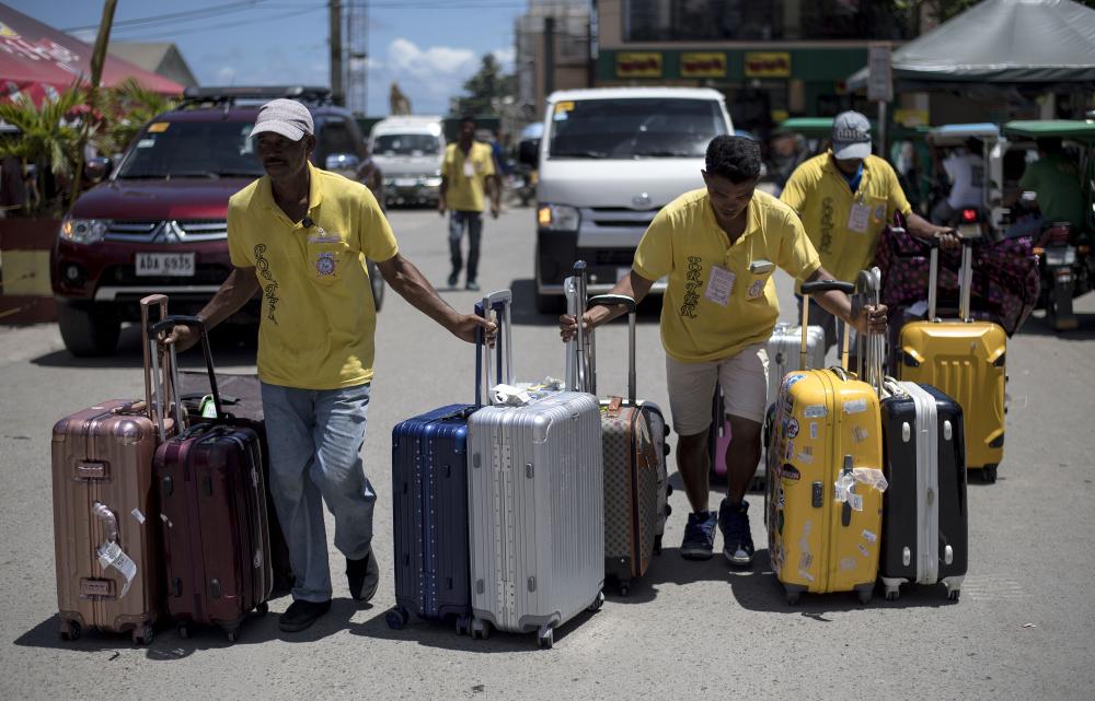 Porters carry the luggage of tourists that came vacationing in Boracay on Tuesday ahead of its closure. — AFP